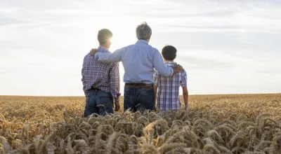 Three generations of farmers standing in a field looking out at the horizon