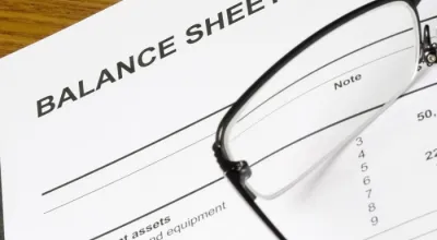 The top left corner of a balance sheet with a pair of glasses laying on top of the paper
